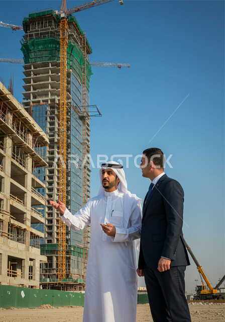 التطور المعماري والحضاري في المملكة العربية السعودية، الاشرف على أعمال البناء والمقاولات والتطوير العقاري، مراقبة تشييد المباني والمشاريع الضخمة، رجل عربي خليجي سعودي يرتدي الغترة والثوب التقليدي يقوم بالشرح لمستثمر اجنبي يرتدي البدلة الرسمية في موقع البناء