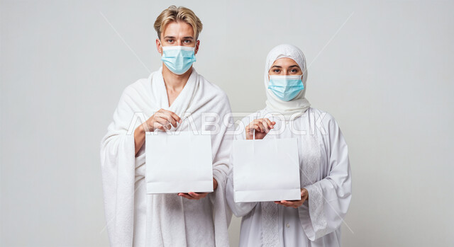 Blank white board, concept of pillars of Islam and performing religious duties, close-up portrait of a pilgrim man wearing ihram clothes and mask standing beside his wife straight holding a white mockup, performing Hajj and Umrah rituals, worship and getting closer to God, following preventive measures from infection, white background