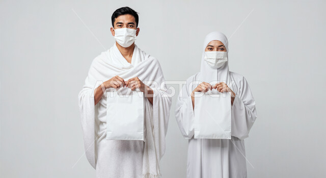 لوحة بيضاء فارغة، مفهوم أركان الإسلام وأداء الفرائض الدينية، بورتريه مقرب لرجل حاج يرتدي ثياب الإحرام والكمامة يقف بجانب زوجته باستقامة يمسكان موك اب ابيض، تأدية مناسك الحج والعمرة، العبادة والتقرب إلى الله، اتباع الاجراءات الوقائية من العدوى، خلفية بيضاء