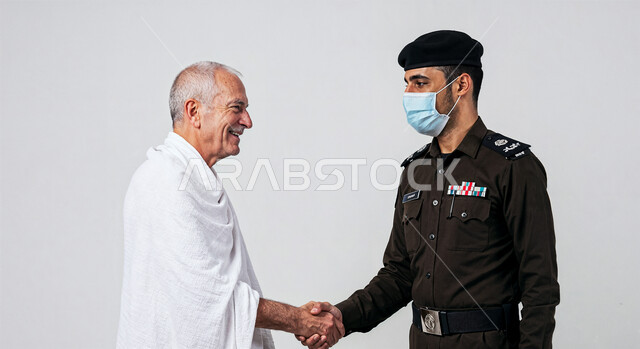 المصافحة والترحيب والسلام، الحفاظ على أمن وأمان الحجاج، بورتريه لرجل أمن عربي خليجي سعودي يرتدي الزي العسكري يقوم بمصافحة حاج يرتدي لباس الاحرام بتعابير الاحترام، أداء مناسك الحج والعمرة، خلفية بيضاء