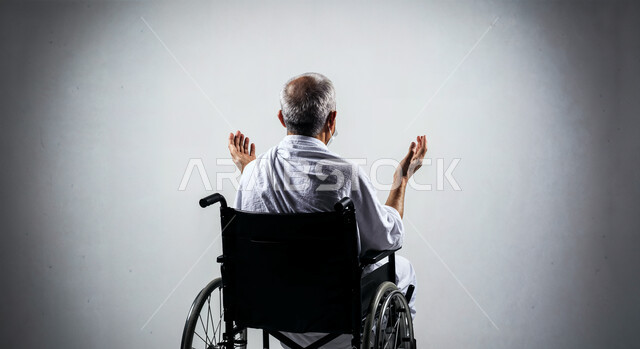 مفهوم أركان الإسلام وأداء الفريضة الدينية، رفع اليدين والدعاء بخشوع وتضرع، بورتريه لحاج من ذوي الهمم يرتدي ثياب الإحرام يجلس على كرسي متحرك يقوم بتأدية مناسك الحج والعمرة، العبادة والتقرب إلى الله، خلفية بيضاء