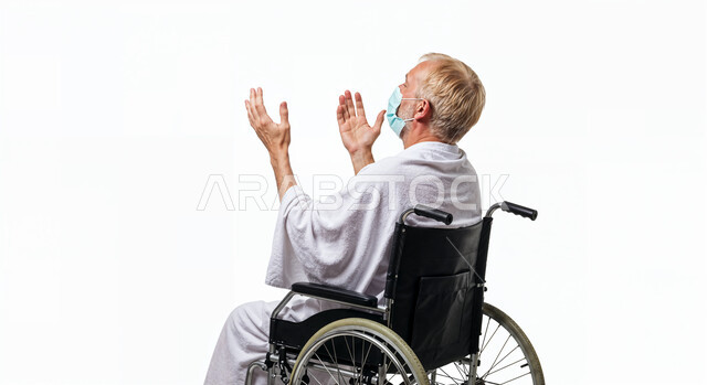 مفهوم أركان الإسلام وأداء الفريضة الدينية، رفع اليدين والدعاء بخشوع وتضرع، بورتريه لحاج من ذوي الهمم يرتدي ثياب الإحرام يجلس على كرسي متحرك يقوم بتأدية مناسك الحج والعمرة، العبادة والتقرب إلى الله، خلفية بيضاء