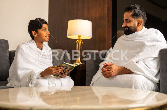تلاوة وقراءة القرآن، أداء مناسك الحج والعمرة، زيارة مكان ومعلم اسلامي ديني مقدس في المملكة العربية السعودية, العبادة والتقرب إلى الله تعالى، رجل عربي خليجي سعودي يرتدي لباس الاحرام يجلس مع ابنه في بهو الفندق، مقصد المسلمين من أنحاء العالم