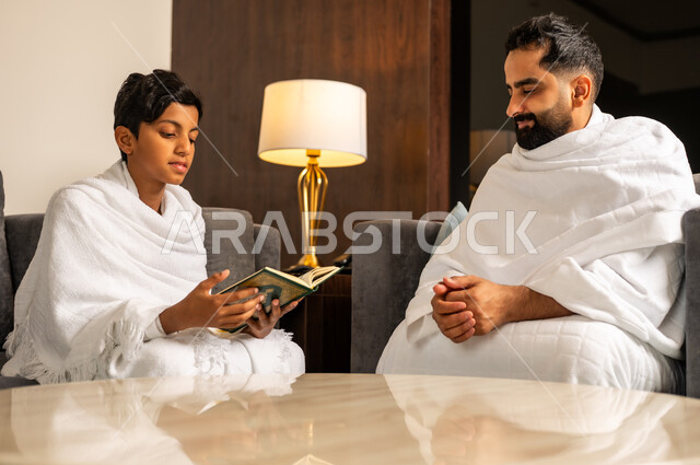 تلاوة وقراءة القرآن، أداء مناسك الحج والعمرة، زيارة مكان ومعلم اسلامي ديني مقدس في المملكة العربية السعودية, العبادة والتقرب إلى الله تعالى، رجل عربي خليجي سعودي يرتدي لباس الاحرام يجلس مع ابنه في بهو الفندق، مقصد المسلمين من أنحاء العالم