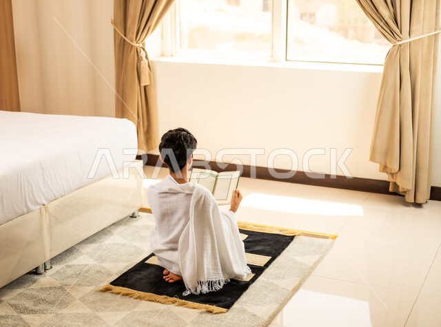 اداء الصلاة على وقتها، العبادة والتقرب إلى الله تعالى، صورة من الخلف لرجل يرتدي ثياب الاحرام يقرأ القرأن الكريم بتعابير الدعاء والتضرع, أداء مناسك الحج والعمرة، مكان ومعلم اسلامي ديني مقدس في المملكة العربية السعودية