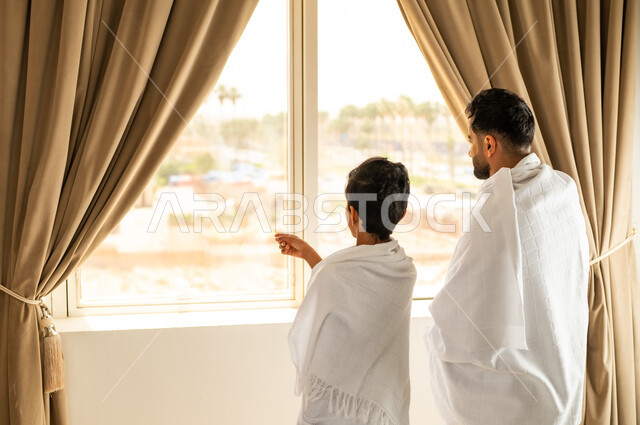 مكان ومعلم اسلامي ديني مقدس في المملكة العربية السعودية, العبادة والتقرب إلى الله تعالى، الاطلالة على جبال مكة المكرمة، صورة من الخلف لرجل عربي خليجي سعودي يرتدي لباس الاحرام يقوم بالدعاء مع ابنه, مقصد المسلمين من أنحاء العالم، أداء مناسك الحج والعمرة