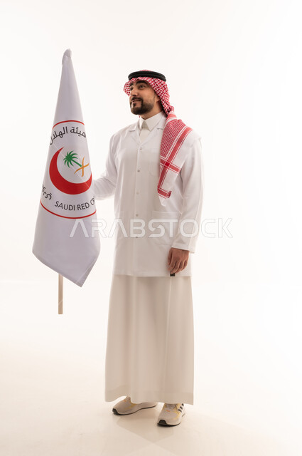 الإسهام في الخدمات الإنسانية والاجتماعية، تقديم الخدمة الطبية الإسعافية الطارئة بالمملكة، علم هيئة الهلال الأحمر السعودي، العمل في المجال الطبي، بورتريه لطبيب سعودي عربي خليجي يرتدي المعطف الأبيض يقف باستقامه بتعابير الثقة بالنفس، الجسم بالطول الكامل، خلفية بيضاء