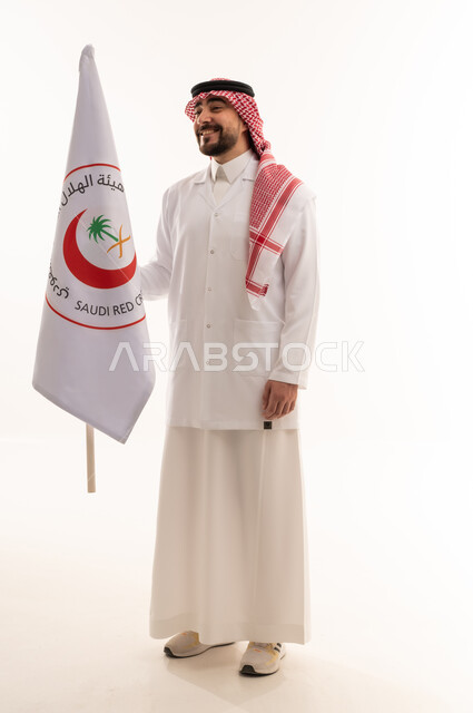 الإسهام في الخدمات الإنسانية والاجتماعية، تقديم الخدمة الطبية الإسعافية الطارئة بالمملكة، علم هيئة الهلال الأحمر السعودي، العمل في المجال الطبي، بورتريه لطبيب سعودي عربي خليجي يرتدي المعطف الأبيض يقف باستقامه بتعابير الثقة بالنفس، الجسم بالطول الكامل، خلفية بيضاء