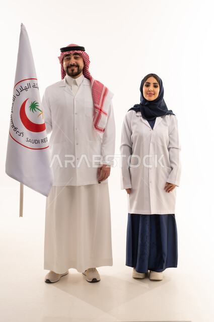 علم هيئة الهلال الأحمر السعودي، العمل في المجال الطبي، بورتريه لطبيبين سعوديين عربيين خليجيين يرتديان المعطف الأبيض يقفان باستقامه بتعابير الثقة بالنفس، الإسهام في الخدمات الإنسانية، تقديم الخدمة الطبية الإسعافية الطارئة، الجسم بالطول الكامل، خلفية بيضاء