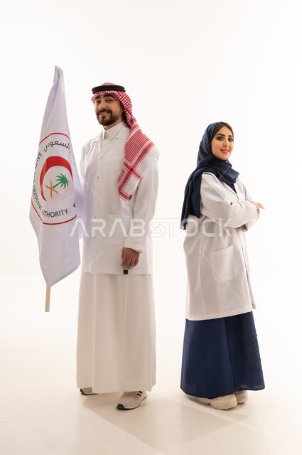 علم هيئة الهلال الأحمر السعودي، العمل في المجال الطبي، بورتريه لطبيبين سعوديين عربيين خليجيين يرتديان المعطف الأبيض يقفان باستقامه بتعابير الثقة بالنفس، الإسهام في الخدمات الإنسانية، تقديم الخدمة الطبية الإسعافية الطارئة، الجسم بالطول الكامل، خلفية بيضاء