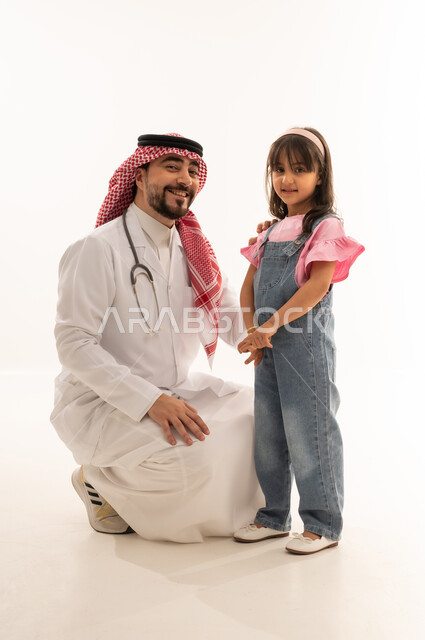 تعابير السرور واللطف، مراكز ومستشفيات العلاج في السعودية، الحاجة إلى العلاج والمساعدة الطبية, بورتريه لطبيب عربي خليجي سعودي يرتدي الثوب التقليدي والشماغ مع المعطف الابيض يقف بجانب فتاة ينظران الى الكاميرا، مهنة ووظيفية طبية، الجسم بالطول الكامل، خلفية بيضاء