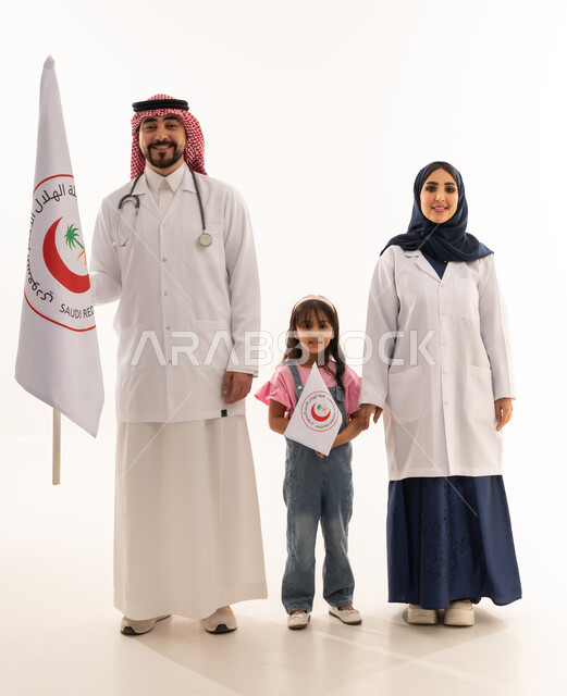 علم هيئة الهلال الأحمر السعودي، العمل في المجال الطبي، بورتريه لطبيبين سعوديين عربيين خليجيين يرتديان المعطف الأبيض يقفان بجانب فتاة تمسك بيدها شعار الهيئة، الإسهام في الخدمات الإنسانية، تقديم الخدمة الطبية الإسعافية الطارئة، الجسم بالطول الكامل، خلفية بيضاء
