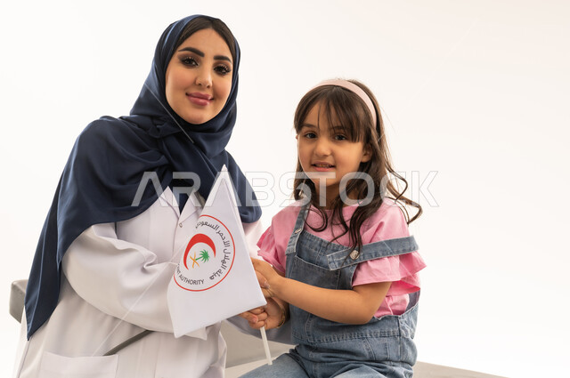 هيئة الهلال الأحمر السعودي، العمل في المجال الطبي والصحي، بورتريه مقرب لطبيبة سعودية عربية خليجية ترتدي المعطف الأبيض تجلس مع فتاة صغيرة تمسك بيدها شعار الهيئة، الإسهام في الخدمات الإنسانية والاجتماعية، تقديم الخدمة الطبية الإسعافية الطارئة بالمملكة، خلفية بيضاء