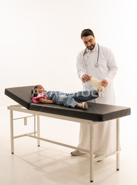 Extremity injuries, hospitals and treatment centers in Saudi Arabia, portrait of a Saudi Arabian Gulf doctor wearing a traditional thobe with a white coat wrapping a bandage on a little girl's foot, medical profession and occupation, white background