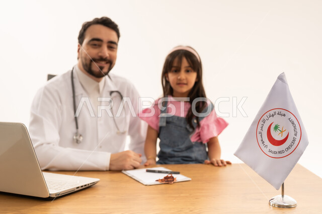 Providing emergency medical services in the Kingdom, integrating technology and technology into the medical and health field, working in the Saudi Red Crescent Authority, portrait of a Saudi Arabian Gulf doctor wearing a white coat sitting with a little girl working on a laptop, white background