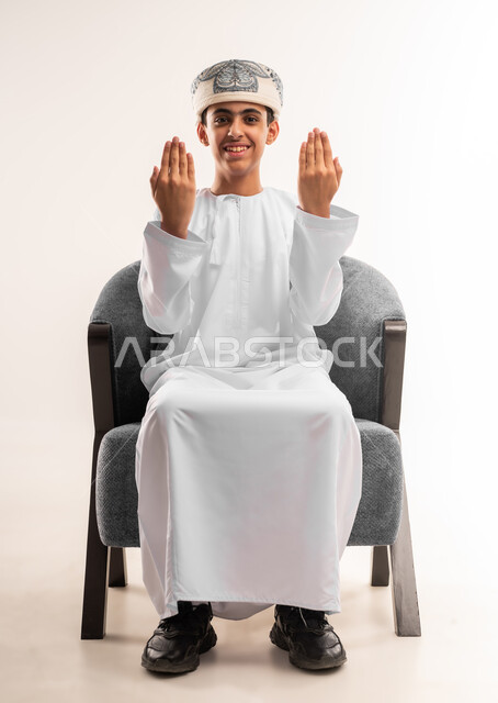 تعابير الرفض والإمتناع، الأمر بالتوقف عن فعل شيء ما، بورتريه لولد عربي خليجي عماني يرتدي الدشداشة و الكمه يضع يده على وجهه ويقوم بالاشارة بإيماءات النهي والشعور بالغضب والانزعاج، صورة الجسم بالطول الكامل، خلفية بيضاء .