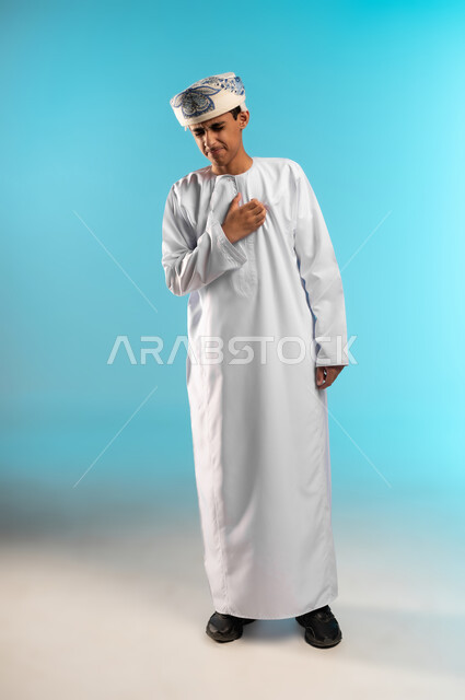 مفهوم الترحيب و السلام ، ايماءات إلقاء التحية، بورتريه لولد عربي خليجي عماني يرتدي الدشداشة و الكمة ، حركات يدين تدل على المصافحة، صورة الجسم بالطول الكامل ، خلفية زرقاء .