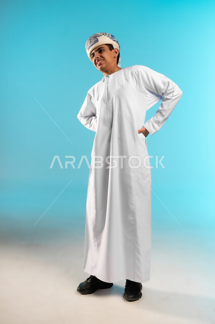 آلام العنق والعمود الفقري, الحاجة للعلاج الفيزيائي، الإحساس بالتعب والإرهاق, وجع مفاصل و عظام الرقبة, بورتريه لولد عربي خليجي عماني يرتدي الدشداشة والكمة يضع يده حول ظهره بإيماءات الألم, الجسم بالطول الكامل, خلفية زرقاء .