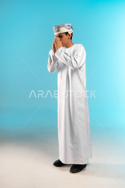 ضرورة أخذ العلاج المناسب، الإرهاق والتعب والحاجة للراحة، العطاس والكحه وأعراض الرشح، الإصابة بالزكام والانفلونزا، بورتريه لولد عربي خليجي عماني يرتدي الدشداشة والكمه العمانية يمسك المنديل الورقي بيده لمنع انتشار العدوى، الجسم بالطول الكامل، خلفية زرقاء .