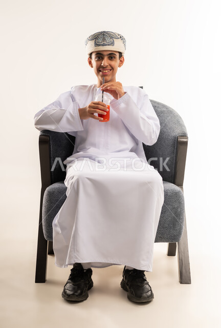 المحافظة على سلامة الجهاز المناعي، فاكهة منعشة ولذيذة، اتباع نظام غذائي صحي، بورتريه لولد عربي خليجي عماني يرتدي الدشداشة والكمة يحمل بيده كوب من العصير الطازج، مفهوم العناية والاهتمام بالصحة, خلفية بيضاء .