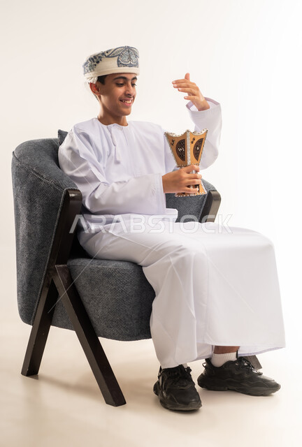 العادات والتقاليد العمانيه, التطيب بالعطور والبخور,بورتريه لولد عربي خليجي عماني يرتدي الدشداشه والكمه يحمل بيده المبخرة ويقوم بالتعطر, الأناقة والاهتمام بالمظهر الخارجي, استخدام خشب العود بالأعياد والمناسبات, خلفيه بيضاء .