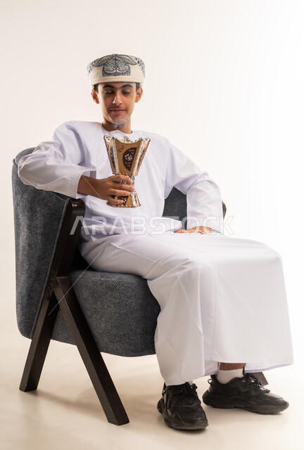 استخدام خشب العود بالأعياد والمناسبات, التطيب بالعطور والبخور, بورتريه لولد عربي خليجي عماني يرتدي الدشداشه والكمه يحمل بيده المبخرة ويقوم بالتعطر, الأناقة والاهتمام بالمظهر الخارجي, العادات والتقاليد العمانيه, خلفيه بيضاء .