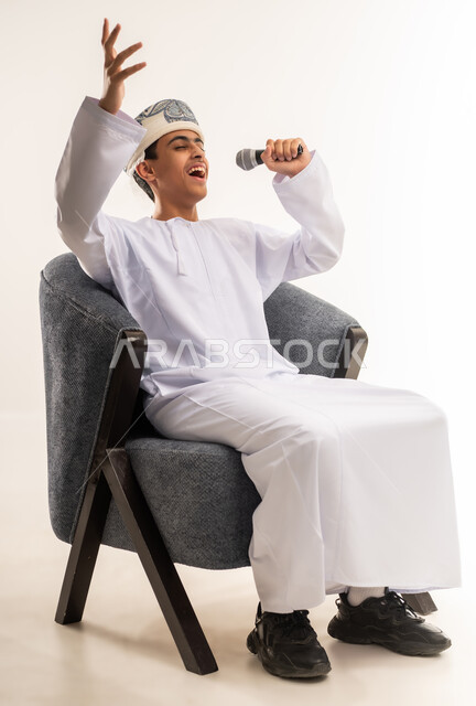 Recording a singing audio clip, expressions of integration and interaction with the music, a portrait of a smiling Omani Gulf Arab boy wearing a kummah and a dishdasha, holding a microphone in his hand, singing, looking at the camera with gestures of joy and happiness, presenting vocal performances, beige background.