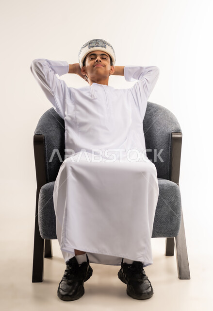 تعابير التأمل والتفكير، الحاجة إلى النوم والشعور بالتعب و الخمول, بورتريه لولد عربي خليجي عماني يرتدي الكمة والدشداشة يجلس على كرسي مريح يضع يديه خلف راسه بإيماءات الراحة والإسترخاء, خلفية بيج .