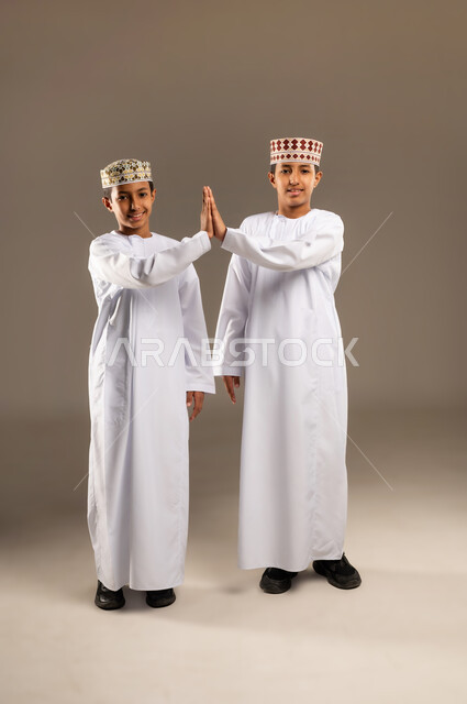 الاتفاق عل شئ ما ، بورتريه لولدان عربيان خليجيان عمانيان يتصافحان بحرارة، ايماءات وجه ويدين تدل على السعادة، العلاقات الاخويه المترابطة، النظر الى الكاميرا بتعابير السرور ، تعارف وصداقات، خلفية بيج .