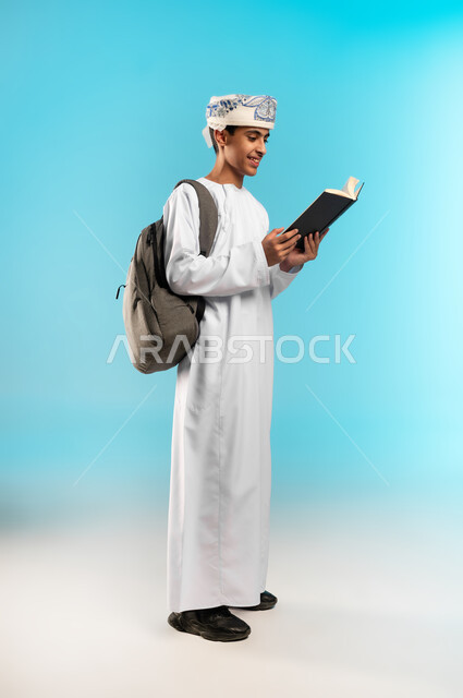 الاهتمام بتصفح الكتب المفيدة، حب المطالعة والقراءة، التعليم في سلطنة عمان, مراجعة الدروس اليومية, مفهوم الاجتهاد والتفوق، بورتريه لطالب عربي خليجي عماني يرتدي الدشداشة والكمة يحمل حقيبة الظهر المدرسية يمسك بيده كتاب ، خلفية ملونه .