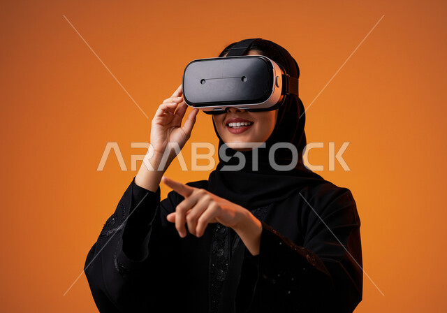 التكنولوجيا الحديثة واستخدام الأجهزة المتطورة، المتعة والتسلية بمحاكاة العالم الخيالي، الاندماج والتفاعل مع الواقع الافتراضي, بورتريه مقرب لامرأة عربية خليجية سعودية محجبة ترتدي نظارة في آر ثلاثية الأبعاد بايماءات التفاعل, خلفية برتقالية