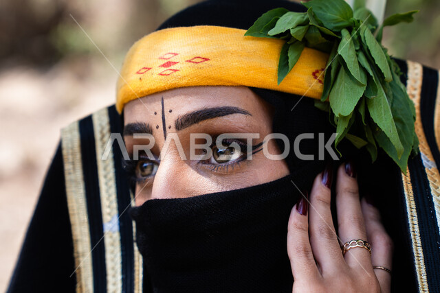 ابراز العيون المكحلة السوداء ، مفهوم الحياء والستر، صورة مقربة لوجه امراه عربية خليجيه سعودية محجبه تقوم بوضع اللثام على وجهها ، نظرات الأنوثه الناعمه، ارتداء الزي الشعبي التقليدي في قرية ذي عين بالباحة