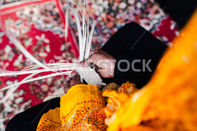 التراث والأصالة في دولة المملكة العربية السعودية, حرف يدوية تاريخية, أعمال وصناعات قديمة, استخدام أوراق النخيل المجففة في صناعة السلل, منتجات محلية وطنية سعودية, مهن شعبية تقليدية, صورة مقربة ليد إمرأة عربية خليجية سعودية تقوم بجدل سعائف الخوص