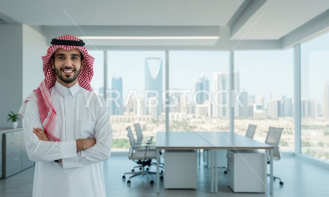 Comfortable work environment in Saudi companies, looking at the camera with expressions of pleasure and happiness, office profession and job, a smiling Saudi Arabian Gulf man wearing a traditional shemagh and thobe standing with crossed hands in gestures of self-confidence inside the office at the company headquarters