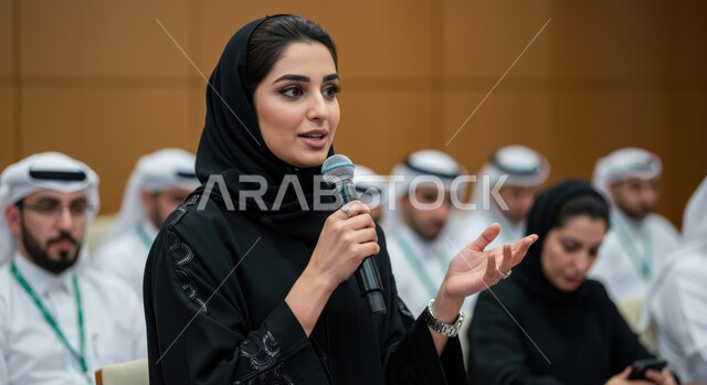 اتقان فن الالقاء والخطابة، مهارات التحدث والحوار، إمرأة عربية خليجية سعودية ترتدي الحجاب والعباءة تمسك بيدها مكبر الصوت تشارك في مؤتمر بإيماءات الاندماج والتركيز والثقة بالنفس
