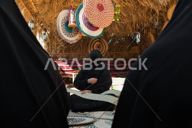 Traditional folk industries, Saudi handicrafts, ancient folk crafts and professions, the craft of making cloaks using colored threads, a Saudi Arabian Gulf woman wearing a burqa knitting and spinning fabrics and cloth