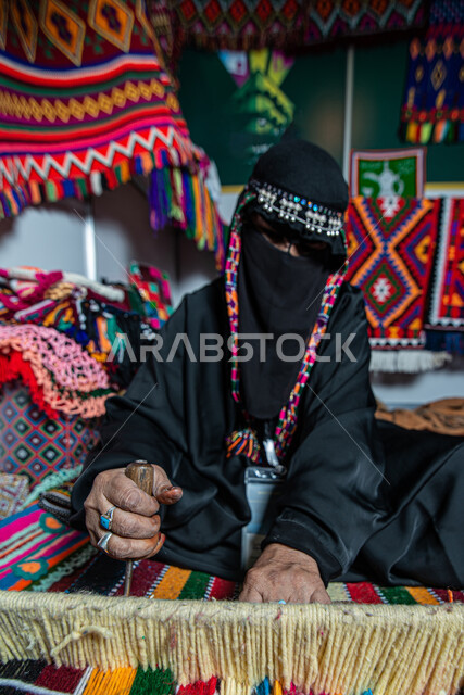 Traditional folk industries, Saudi handicrafts, ancient folk crafts and professions, the craft of making cloaks using colored threads, a Saudi Arabian Gulf woman wearing a burqa knitting and spinning fabrics and cloth