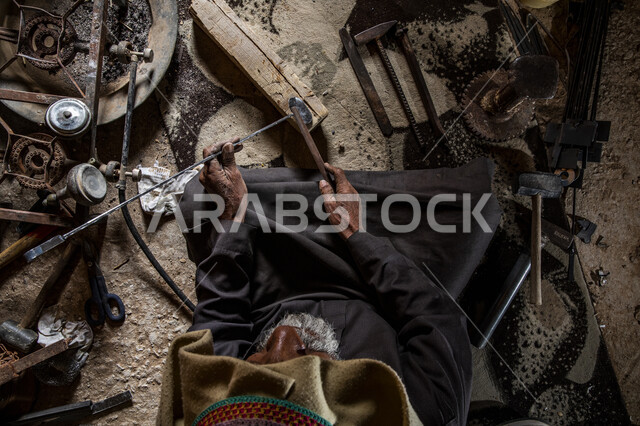 Simple melting and cooling process, a traditional handicraft in Saudi Arabia, method of producing steel and various metals, fire-making on wood, vertical overhead view of a Saudi Arabian Gulf man melting iron and pouring it into special molds and primitive tools