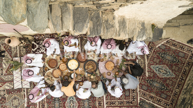 عزيمة غداء شعبية، صورة علوية عامودية لمجموعة من الرجال العرب الخليجيين السعوديين يرتدون الزي التقليدي يجلسون حول مائدة الطعام، اطباق عربية تقليدية سعودية اصيلة
