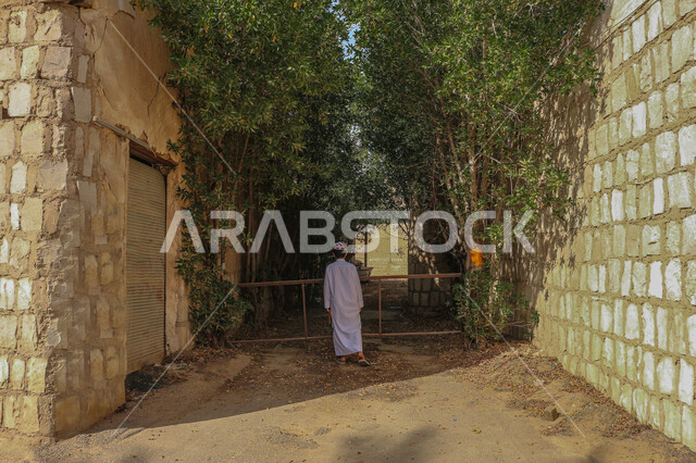 الطراز العربي المعماري القديم، معالم وأماكن تاريخية تراثية مشهورة، البيوت والمباني الطينية البسيطة، صورة من الخلف لرجل عربي خليجي سعودي يرتدي زي شعبي يقف في منزل من الطوب في إحدى الأحياء الشعبية في قرى المملكة العربية السعودية