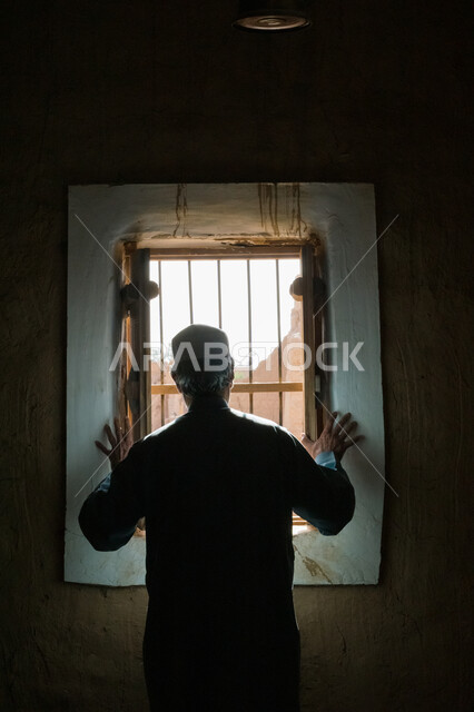 الطراز العربي المعماري القديم، معالم وأماكن تاريخية تراثية مشهورة، البيوت والمباني الطينية البسيطة، صورة من الخلف لرجل عربي خليجي سعودي يرتدي زي شعبي يقف في منزل من الطوب في إحدى الأحياء الشعبية في قرى المملكة العربية السعودية