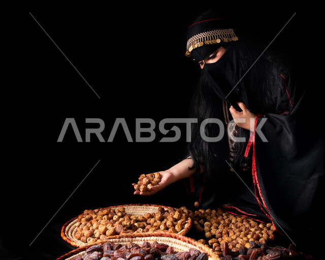 التمر السكري الصحي الطازج في سلل قش، وجبة ذات قيمة غذائية عالية، ضيافة رمضانية لذيذة، انواع من التمور الصحية، صورة مقربة لإمرأة عربية خليجية سعودية ترتدي البرقع والعباءة تمسك بيدها رطب من نخيل المملكة العربية السعودية