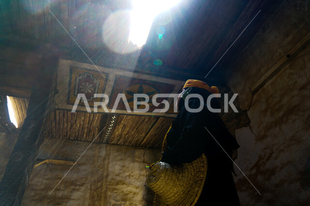 الطراز العربي المعماري القديم، معالم وأماكن تاريخية تراثية مشهورة، البيوت والمباني الطينية البسيطة، إمرأة عربية خليجية سعودية ترتدي الحجاب والعباءة مع البرقع تقف في منزل من الطوب في إحدى الأحياء الشعبية في قرى المملكة العربية السعودية