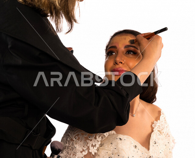بورتريه لعروسة عربية خليجية سعودية جميلة  تضع المكياج بيد فنانة مكياج ، إستخدام إحدى أدوات التجميل في تزيين العروس ، جلسة تصوير رائعة لتجهيز عروسة سعودية ، ترتدي بدلة الزفاف البيضاء ، ليلة العمر ، مناسبات وأفراح ، أدوات مكياج تتوريال ، خلفية بيضاء