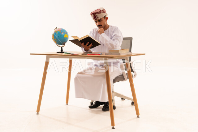 مفهوم التعلم والتفوق والاجتهاد، مراجعة الدروس اليومية، قضاء أوقات الفراغ بالأنشطة المفيدة, بورتريه لطالب جامعي عربي خليجي عماني يرتدي الكمه والدشداشه يجلس على الطاولة يقوم بقراءة الكتاب بايماءات الاندماج, خلفية بيضاء