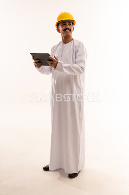 Watching interesting movies and series, spending free time learning and culture, hobby of reading and exploration, portrait of a university engineering student wearing the Saudi Arabian Gulf dress and helmet holding a portable tablet in his hand and looking at something, full body, white background