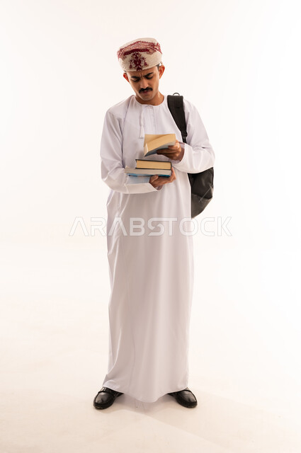 تدوين الملاحظات وكتابة تقارير وأبحاث علمية، بورتريه لطالب جامعي عربي يرتدي الزي الخليجي عماني و يحمل بيده كتب، التعليم الجامعي في عمان ، إيماءات وجه ويدين تدل على التذمر والشعور بالإحباط والحزن من الضغط الدراسي ، الجسم بالطول الكامل، خلفية بيضاء