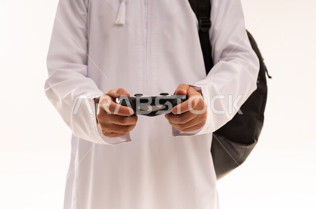 إستخدام أجهزة تقنية حديثة ، ألعاب البلايستيشن الترفيهية والممتعة ، بورتريه مقرب  لشاب عربي عماني خليجي يرتدي الزي التقليدي يمسك بيده عصا التحكم و يلعب بألعاب الفيديو ، مفهوم الفوز والخسارة ، قضاء وقت ممتع ، الجسم بالطول الكامل، خلفية بيضاء