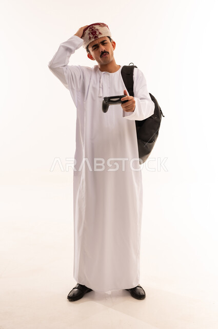 قضاء وقت ممتع ، بورتريه شاب عربي عماني خليجي يرتدي الزي التقليدي يمسك بيده عصا التحكم و يلعب بألعاب الفيديو ، إيماءات وجه ويدين تدل على الإندماج والتفاعل مع اللعبة ، ألعاب البلايستيشن الترفيهية والممتعة ، مفهوم الفوز والخسارة ، الجسم بالطول الكامل، خلفية بيضاء