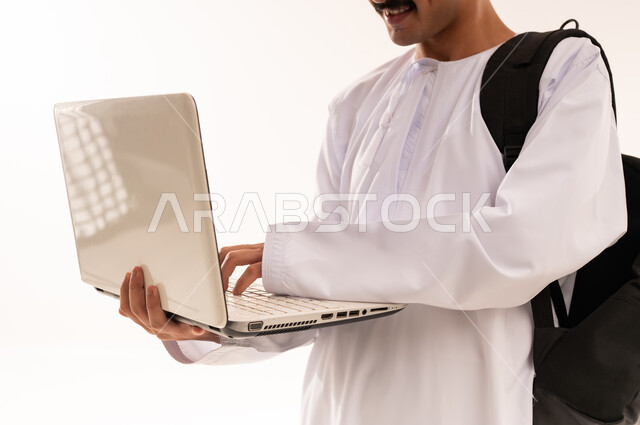 استخدام الأجهزة التقنية الحديثة لحضور المحاضرات الجامعية، التعليم عن بعد عن طريق الانترنت، المناهج والمواد التعليمية في عمان , بورترية مقرب لشاب عربي خليجي عماني يرتدي الدشداشة و الكمه و الحقيبه يقوم بمتابعة الدراسة عبر الحاسب، الجسم بالطول الكامل، خلفية بيضاء